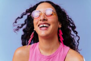 Woman with diastema wearing pink lightning bolt earrings and glasses smiling